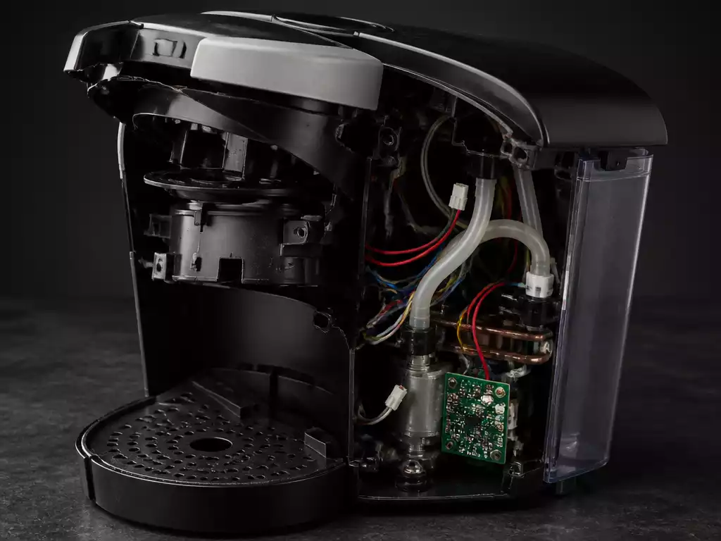 Close-up of a broken Keurig coffee maker with visible internal components, on a dark countertop, symbolizing e-waste