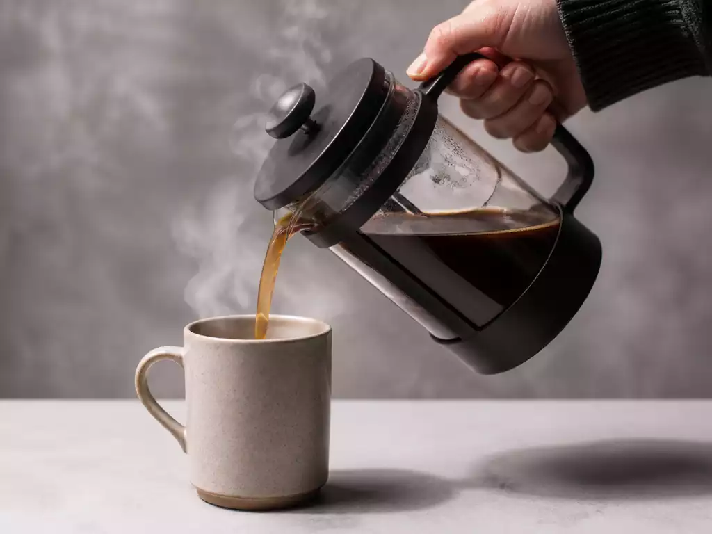 French Press coffee maker in use, pouring rich coffee into a mug