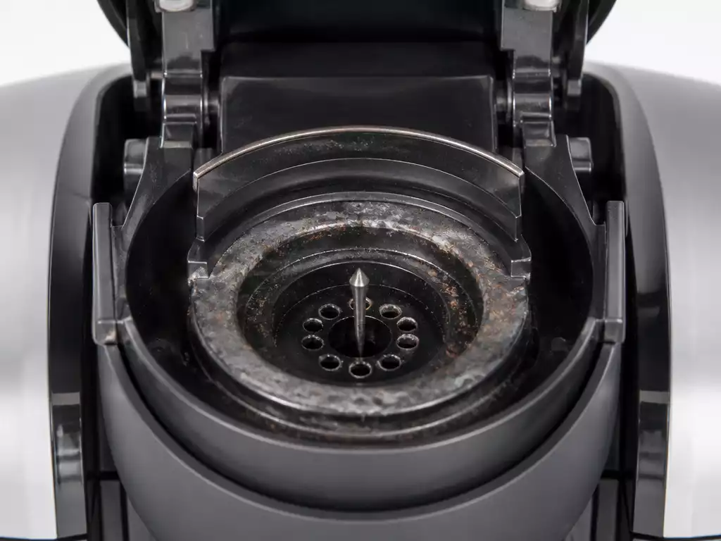 Close-up of a Keurig coffee maker's brew head with a needle, showing potential coffee ground residue or mineral buildup