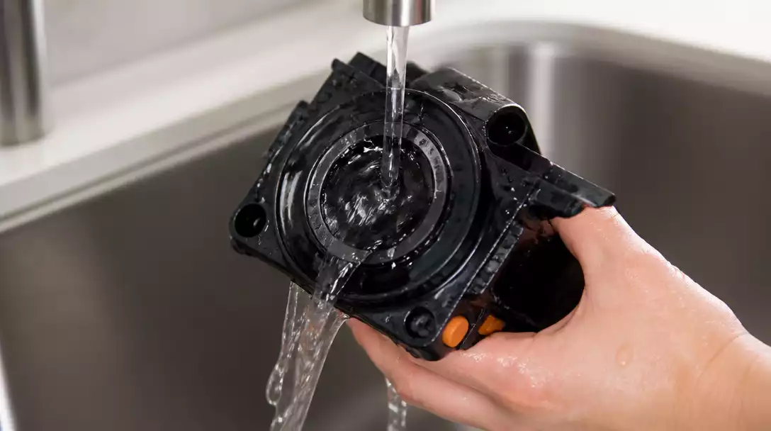 De'Longhi coffee maker brewing unit being cleaned with water